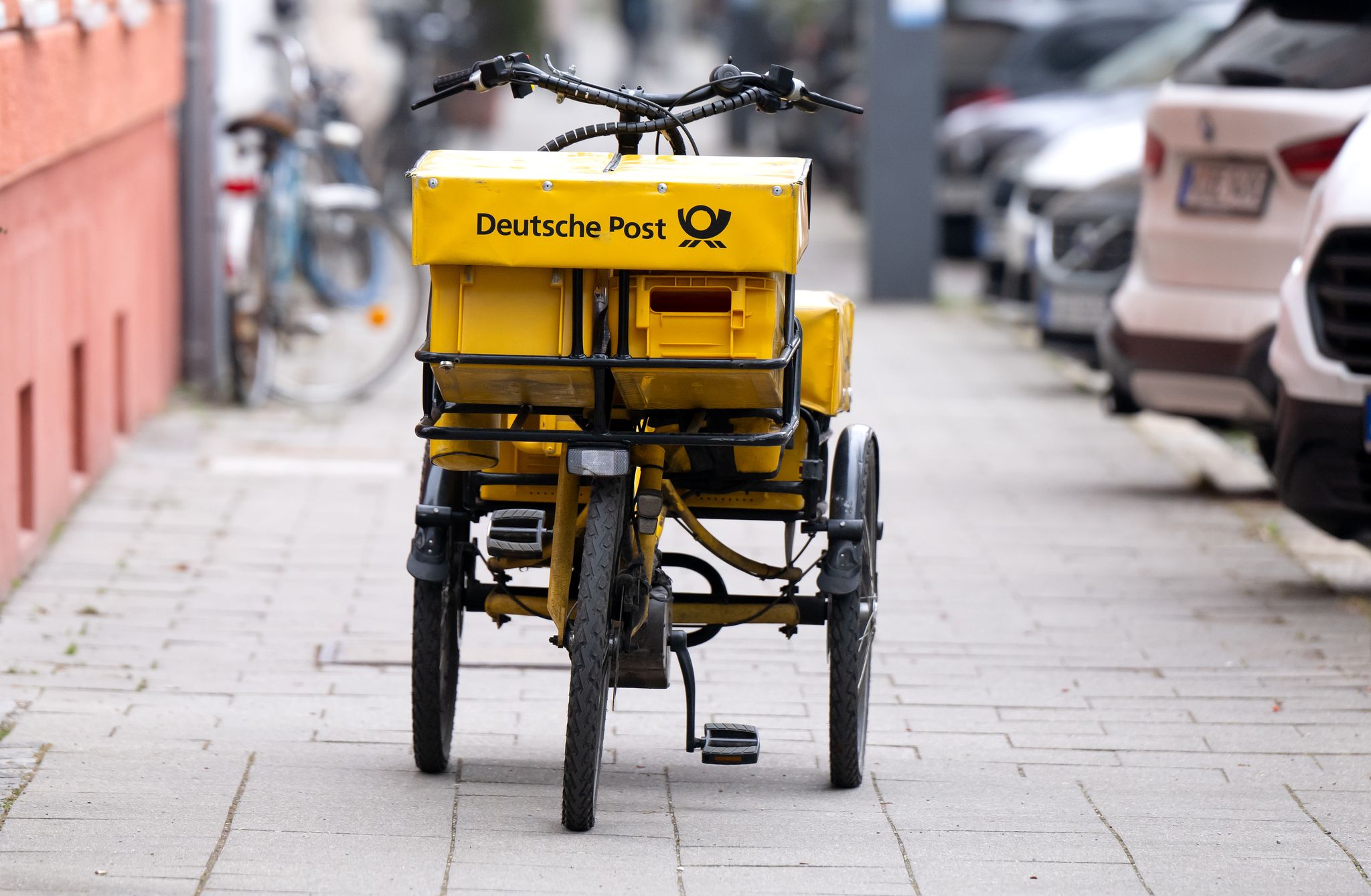 Ein Fahrrad eines Briefträgers steht auf einem Gehweg - auch dieser Briefträger möchte vermutlich gern deutlich besser bezahlt werden.