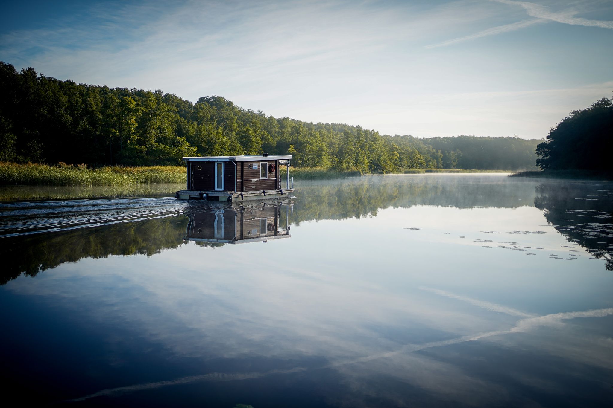 Schönes Revier in Brandenburg: Ein Hausboot fährt am frühen Morgen im Sonnenschein über die Havel.