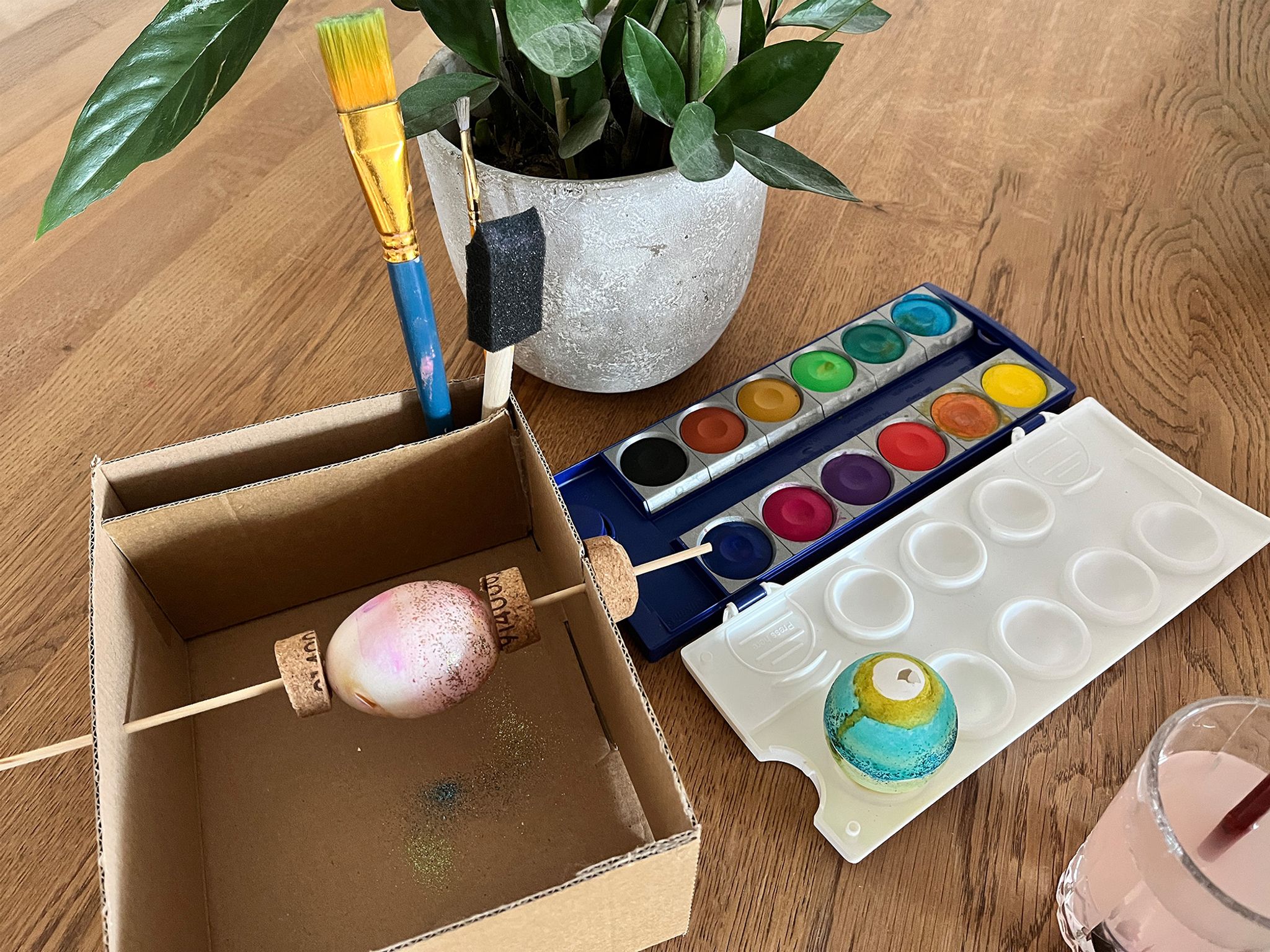 Drehen statt kleckern: Mit Holzspieß, Korken und Karton entsteht eine Mal-Station für Ostereier.