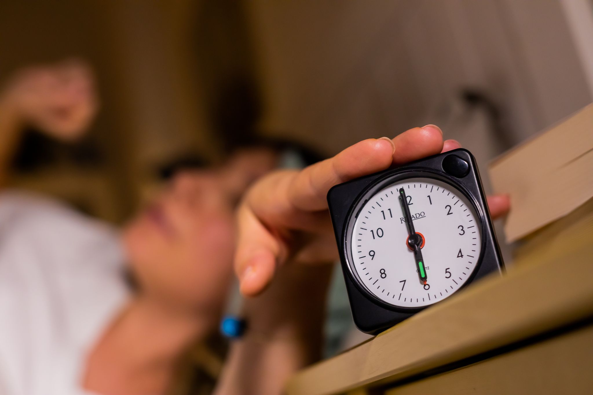Eine Frau schaltet vom Bett aus einen auf sechs Uhr gestellten Wecker aus.