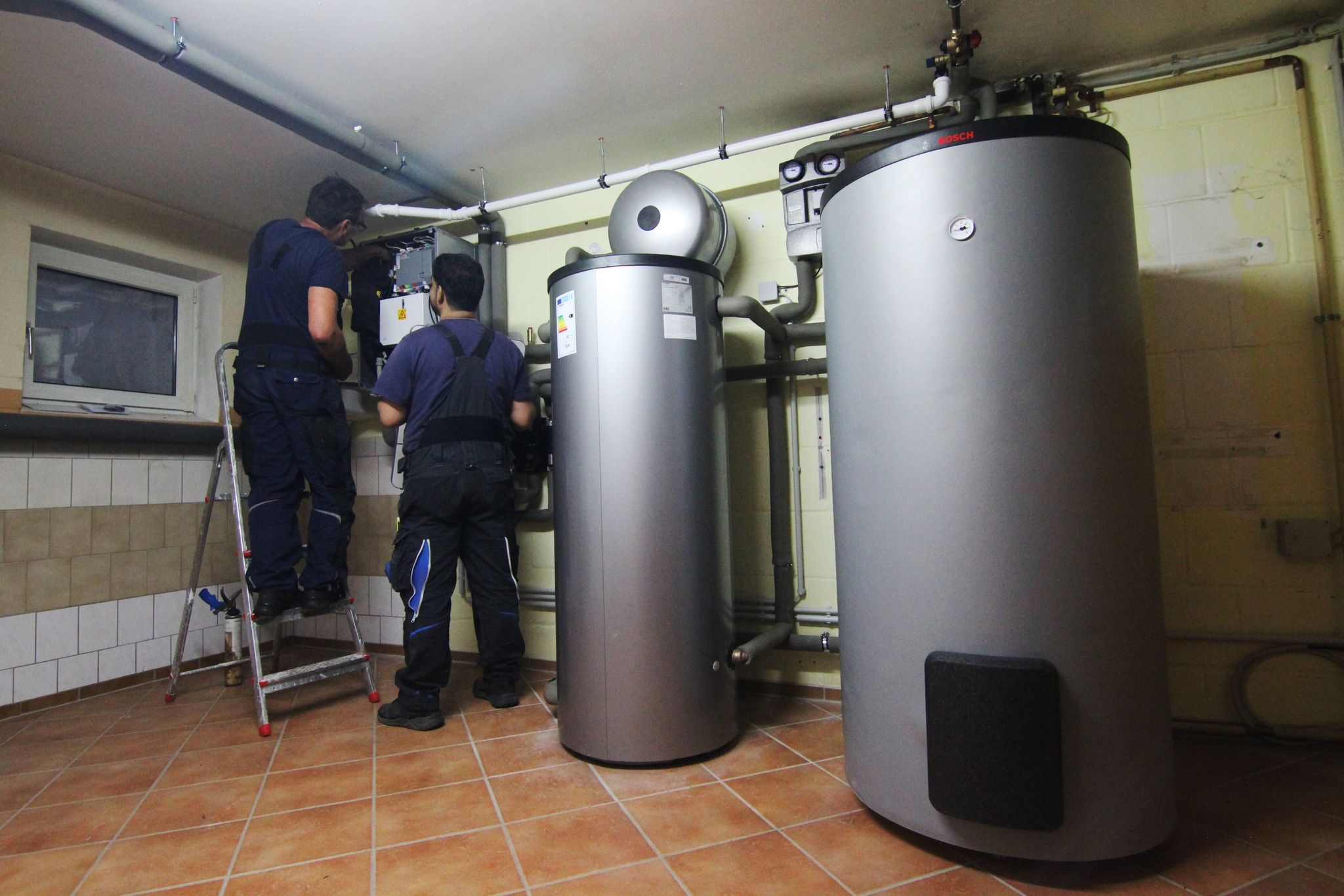 Zwei Handwerker stellen eine Wärmepumpe im Keller einer Doppelhaushälfte ein.