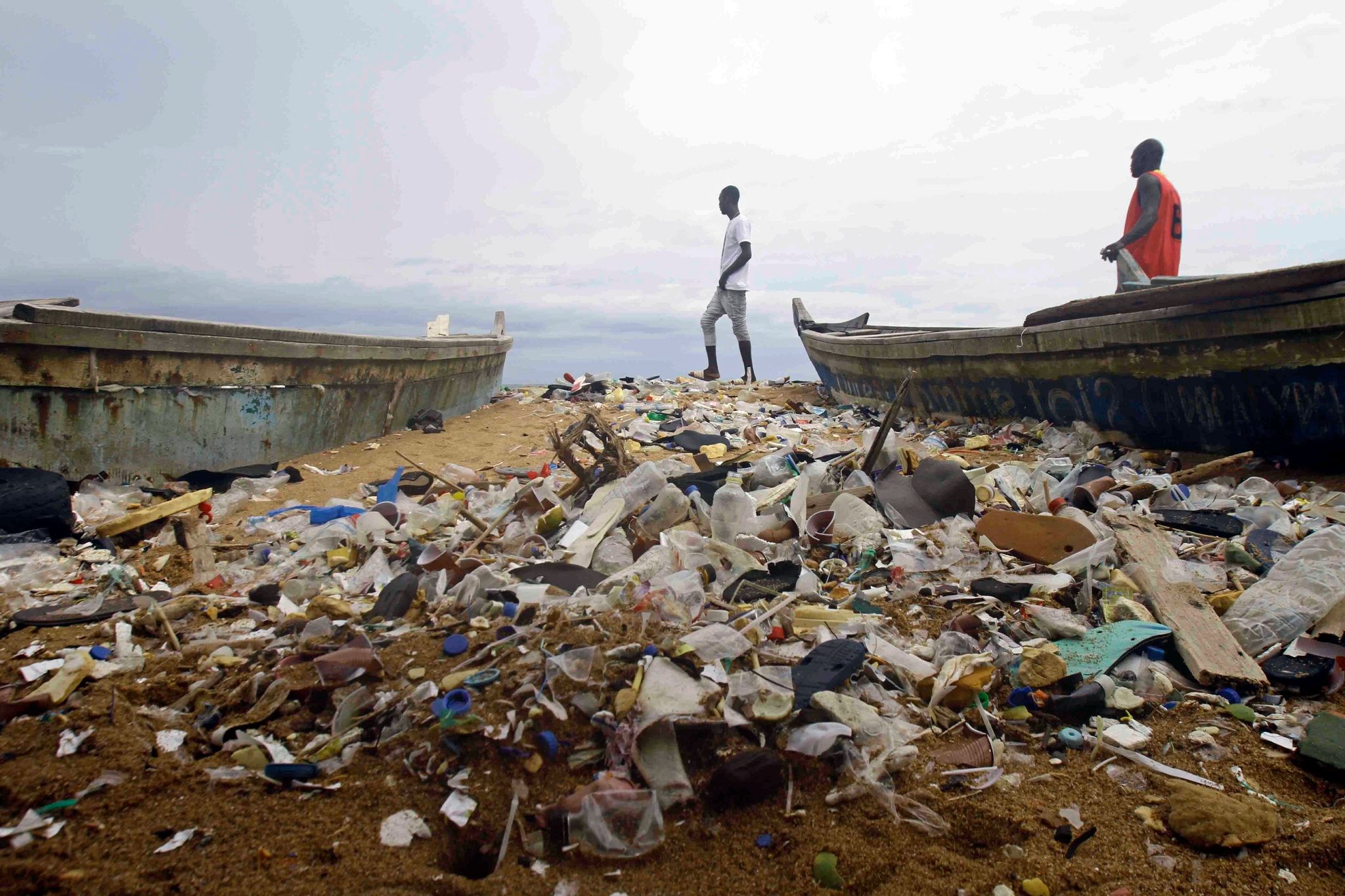 Menschen spazieren über einen mit Plastik verschmutzten Strand an der Elfenbeinküste.